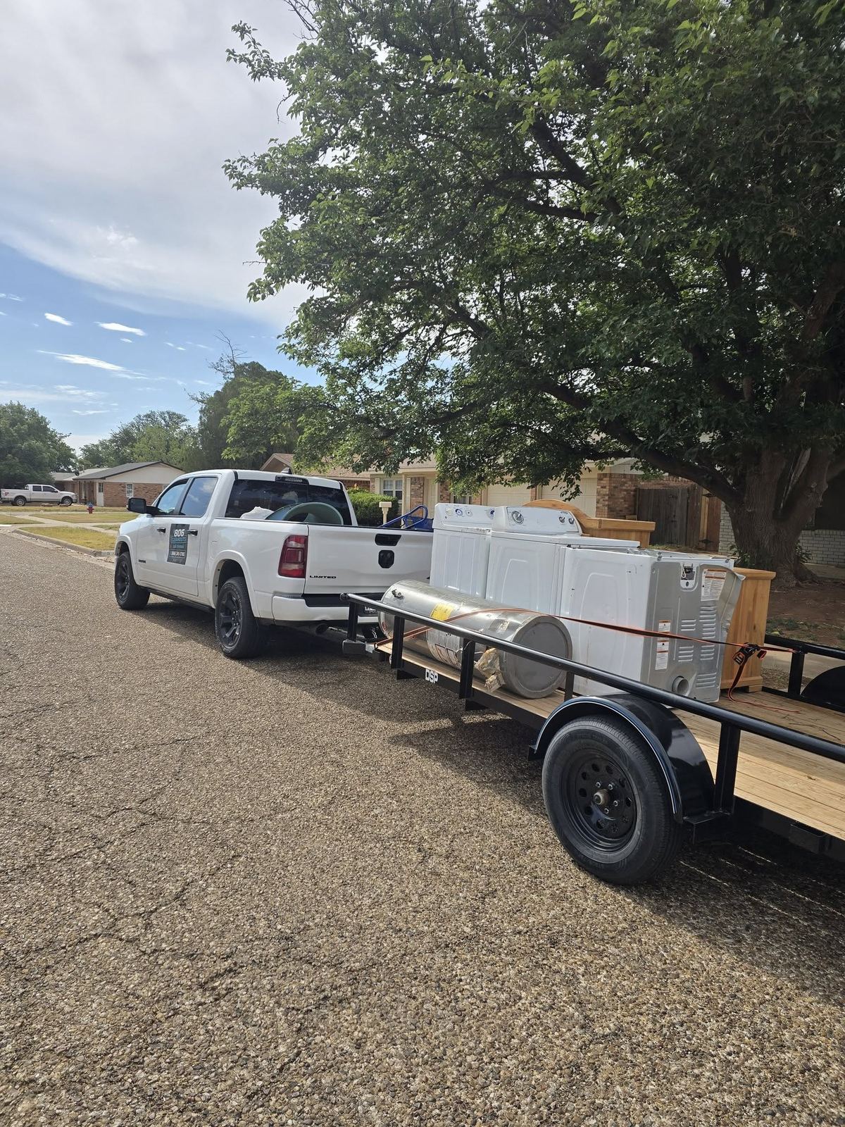 806 Cleanouts truck and trailer loaded with white appliances, parked on a residential street beside a big shade tree